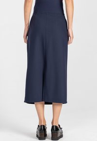 Granatowe spodnie kuloty z wysokim stanem, plisowanym fasonem i gładką teksturą, zestawione z czarnymi platformami o błyszczącym wykończeniu.