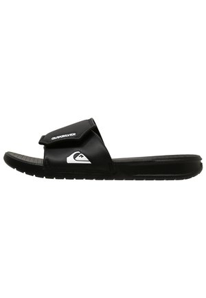 Svart halksandals med en strukturerad sula. Har ett vadderat rem med kardborrestängning och en vit logotyp på den övre delen.