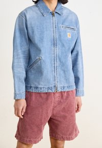 Leren spijkerjack in lichtblauw met een rits aan de voorkant, borstzak en zijzakken, gecombineerd met bordeauxrode shorts. Gladde textuur, casual ontwerp.