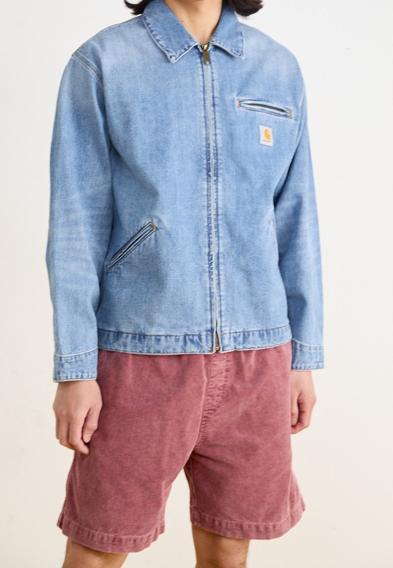 Leren spijkerjack in lichtblauw met een rits aan de voorkant, borstzak en zijzakken, gecombineerd met bordeauxrode shorts. Gladde textuur, casual ontwerp.