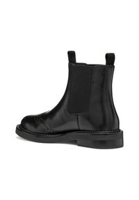 Stivale Chelsea in pelle nera con pannelli laterali elastici, punta tonda, dettagli brogue e una spessa suola in gomma nera.