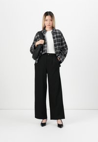 Oversized košile s černobílým kostkovaným vzorem, bílý fitted top, černé kalhoty s vysokým pasem a širokými nohavicemi, a černé špičaté baleríny. Minimalistický design.
