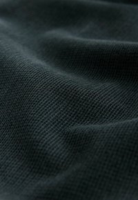 Dark green textured fabric with a waffle weave pattern, showcasing a soft and slightly wrinkled surface. Lightweight and breathable material.