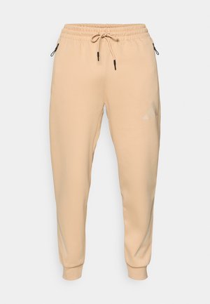 Smėliniai sportiniai kelnes, pagamintos iš minkštos medžiagos, su elastinga liemene ir raišteliu, šoninėmis kišenėmis ir subtiliu logotipu ant šlaunies.