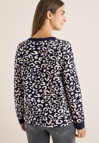 Suéter marino con un patrón de leopardo crema, cuello redondo, mangas largas y puños acanalados; tejido suave y texturizado.