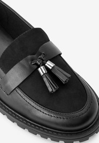 Czarne skórzane loafersy zamszową cholewką, szerokim paskiem, frędzlami i wytrzymałą podeszwą z widocznym wzorem bieżnika.