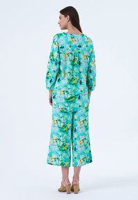 Een bijpassende outfit bestaande uit een lange mouw top en brede broek in een teal en gele bloemenprint, met een ontspannen pasvorm en zachte stof.