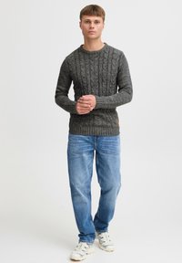Dark gray cable knit sweater with ribbed hem, paired with light blue denim jeans. Model stands with hands clasped, wearing athletic shoes.