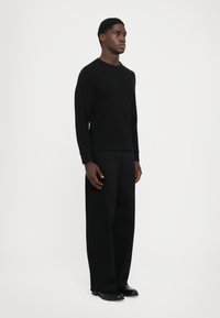 Black long-sleeve shirt with a round neckline paired with wide-leg black trousers. Smooth texture, casual fit, and minimalistic design.