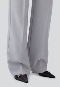 Pantaloni gri cu croială largă, dintr-un material neted, cu o potrivire pe măsură, asociați cu pantofi negri, cu vârf ascuțit, care au cusături decorative.