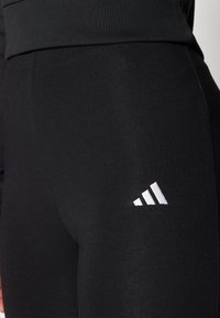Svarta atletiska leggings med en slät yta, med en framträdande vit Adidas-logotyp på underbenet och en bred elastisk midja.