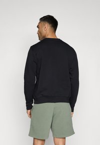 Μαύρη φούτερ μπλούζα με ραμμένα μανίκια και μύτη, φτιαγμένη από υφή ύφασμα. Συνδυασμένη με ανοιχτό πράσινο σορτς, δημιουργώντας μια άνετη εμφάνιση.