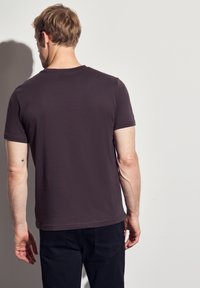 Krátký rukáv, tmavě šedé tričko vyrobené z hladkého materiálu. Jednoduchý design zahrnuje kulatý výstřih a rovný střih, s minimálními detaily.