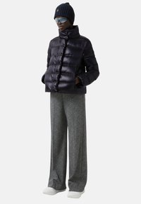 Kurtka puchowa z błyszczącego czarnego materiału z wysokim kołnierzem, zestawiona z szerokimi spodniami w szary wzór i białymi sneakersami, uzupełniona czapką beanie i okularami przeciwsłonecznymi.