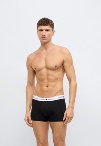 Black boxer briefs with a white waistband featuring the "TOMMY HILFIGER" logo; soft material, fitted design, and mid-thigh length.