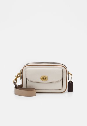 Compact beige leather crossbody bag with front pocket, gold turn-lock clasp, and adjustable strap with a dark tag attached.