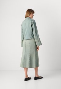 Lyseblå denimjakke med vide ermer, kombinert med et matchende knelangt skjørt. Begge plaggene har synlige sømdetaljer. Svarte leiligheter.