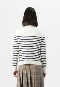 Langärmeliger cremafarbener Pullover mit marineblauen Streifen, runder Ausschnitt und gerippten Bündchen, kombiniert mit einem karrierten Rock in Beige- und Brauntönen.