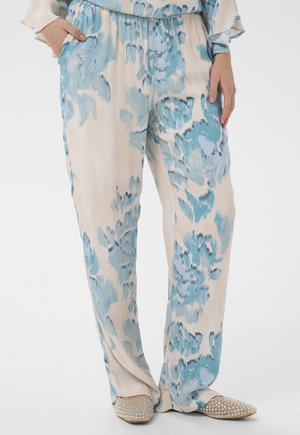 Luźne beżowe spodnie w niebieski kwiatowy wzór, z elastycznym pasem, ręce w kieszeniach, w połączeniu z beżowymi, spiczastymi balerinami ozdobionymi cyrkoniami.
