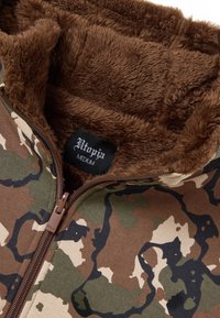 Giacca con zip mimetica con morbido rivestimento in pelliccia marrone visibile all'interno del colletto, etichettata "Utopia Medium."