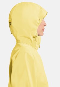 Gelbe wasserdichte Jacke mit Kapuze, die eine glatte Textur und verstellbare Zugbänder aufweist, seitlich vor einem weißen Hintergrund dargestellt.