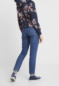 Sudadera de estampado floral en color navy con mangas largas, combinada con jeans azules y zapatillas altas navy. Enfoque en el patrón floral y el ajuste casual.