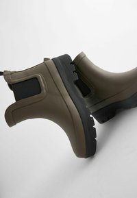 Bottines étanches vert olive avec surface en caoutchouc texturé, semelle extérieure noire et panneaux latéraux élastiques pour un enfilage facile.