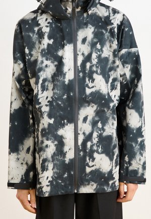 Vooraanzicht van een waterdichte jas in zwart-wit tie-dye patroon, met een ritsluiting, capuchon en een losse pasvorm. Zachte textuur en lange mouwen.