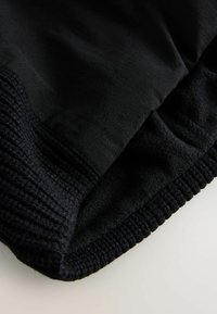 Felpa nera caratterizzata da un tessuto liscio con orlo a coste. La texture è morbida e la costruzione comprende un rivestimento in felpa.