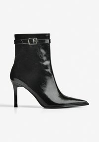 Cizmă de gleznă neagră, din piele lacuită lucioasă, cu vârf ascuțit, toc subțire stiletto și curea decorativă cu cataramă.