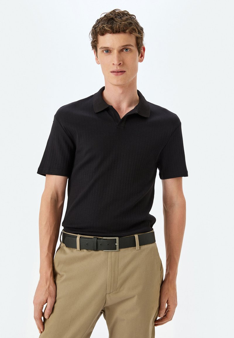Schwarzes, geripptes Poloshirt mit kragenförmigem Ausschnitt, kurzen Ärmeln, kombiniert mit khakifarbenen Hosen und einem schwarzen Gürtel. Einfaches Design, klare Linien.