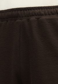 Joggeurs marron foncé en tissu doux et texturé. Caractéristiques : ceinture élastique et détails sur la couture latérale.