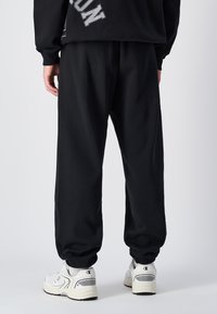 Zwarte sweatpants van katoen met een relaxte pasvorm en geribbelde enkels, gecombineerd met witte sport sneakers met subtiele ontwerpaccenten.