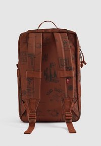 Sac à dos en tissu marron avec des impressions graphiques, des bretelles ajustables, une poigné supérieure et deux boucles latérales. Forme plate avec des coutures renforcées.