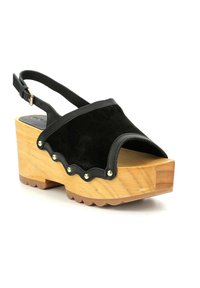 Sandali platform slingback in suede nero con base in legno. Presentano bordi scallopati e borchie dorate lungo il bordo superiore. Dettagli in gros-grain.