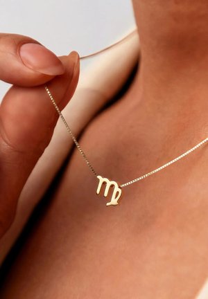 Main tenant un pendentif en or du signe du zodiaque Vierge sur une fine chaîne portée autour du cou d'une personne.