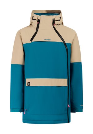 Kind met een blauw-beige winterjas, beige broek, zwarte handschoenen, zwarte laarzen en een blauw gebreide muts, staand en glimlachend.