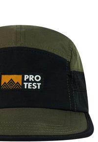 Gorra verde y negra con un parche rectangular que muestra un logo de montaña naranja y el texto blanco "PRO TEST" en el panel frontal.