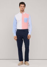Overhemd met knopen en een kleurblokontwerp in koraal, lichtblauw en wit, met een borstzak. Gecombineerd met marineblauwe broek en beige schoenen.
