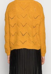 Strickpullover in Senfgelb mit einem strukturierten Zickzackmuster und durchbrochenen Details. Er hat eine legere Passform und einen gerippten Saum.