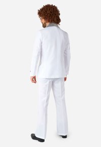 Costume blanc à texture lisse, avec un accent de col métallique. Les pantalons sont évasés en bas. Des chaussures noires viennent compléter le look.