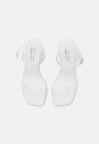 Sandales blanches à talons avec des brides transparentes, un bout carré et une finition lisse ; bride de cheville ajustable avec boucle en métal.