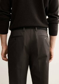 Pantalons gris foncé en tissu texturé, avec deux poches arrière à boutons et une ceinture lisse. Design ajusté.