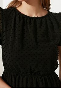 Vestido negro hecho de tela texturizada con pequeños puntos elevados, escote recogido y cintura elástica, con mangas cortas abullonadas.