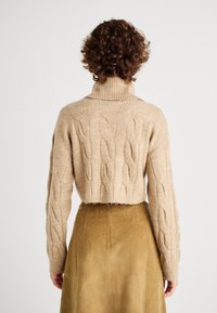 Maglione corto beige a maglia rasata con colletto alto, caratterizzato da motivi testurizzati; abbinato a una gonna in velluto a coste verde oliva.
