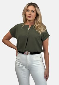 Oliwkowa bluzka z krótkim rękawem z detalem z guzikami, połączona z białymi spodniami z wysokim stanem i czarnym paskiem z srebrną klamrą z logo.