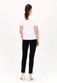 T-shirt bianco a maniche corte con scollo rotondo, abbinato a pantaloni neri attillati e sandali con tacco a blocco oro, visto da dietro.