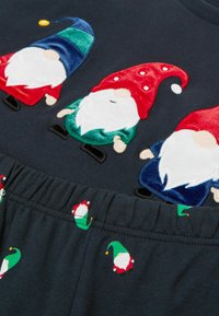 Černý top s třemi barevně vyšitými trpaslíky v červené, zelené a modré barvě. Pás má malé zelené čepice elfů s červenými detaily.