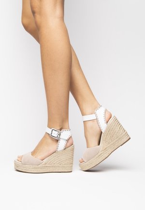 Sandales compensées en daim beige avec brides blanches autour de la cheville, semelle intermédiaire en jute tressé, design à bout ouvert et coutures décoratives le long des brides.