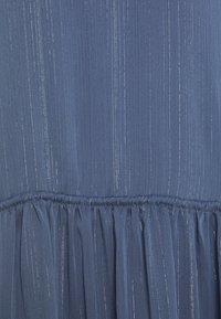 Tissu bleu avec des rayures métalliques argentées verticales et un détail de couture froncée près du bord inférieur.